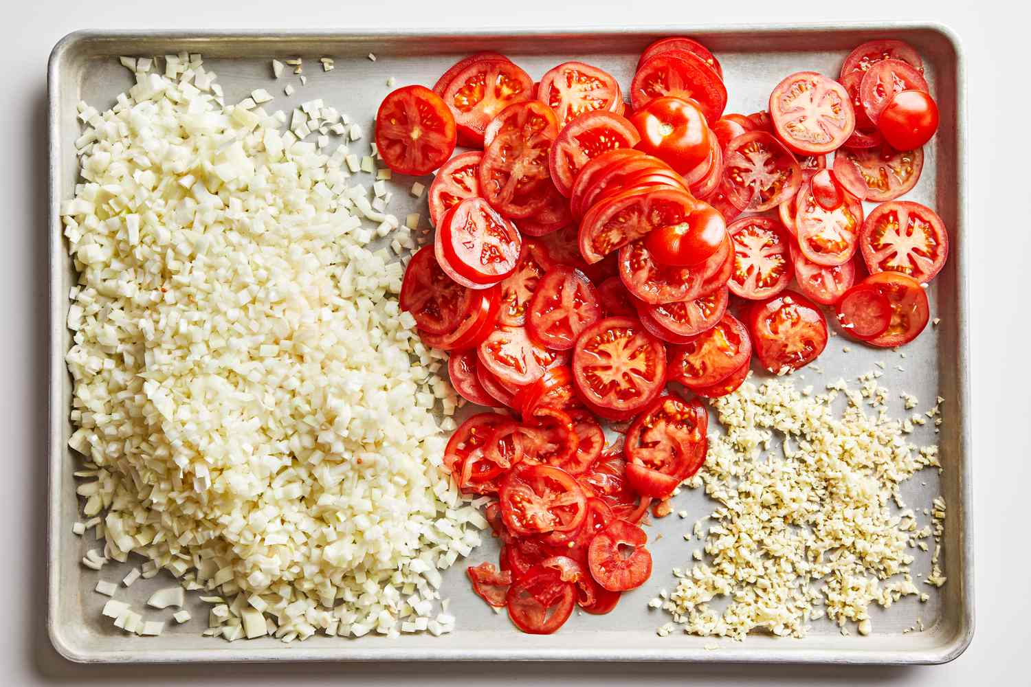 Diced onion and sliced tomatoes on a baking sheet