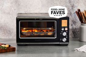 A Breville Smart Oven Air Fryer displayed on a kitchen countertop with a metal basket full of potato wedges baking inside 