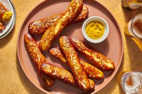 A large plate with German soft pretzel sticks served with mustard and glasses of beer