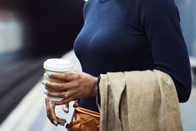 A person commutes on a train holding a cup of coffee