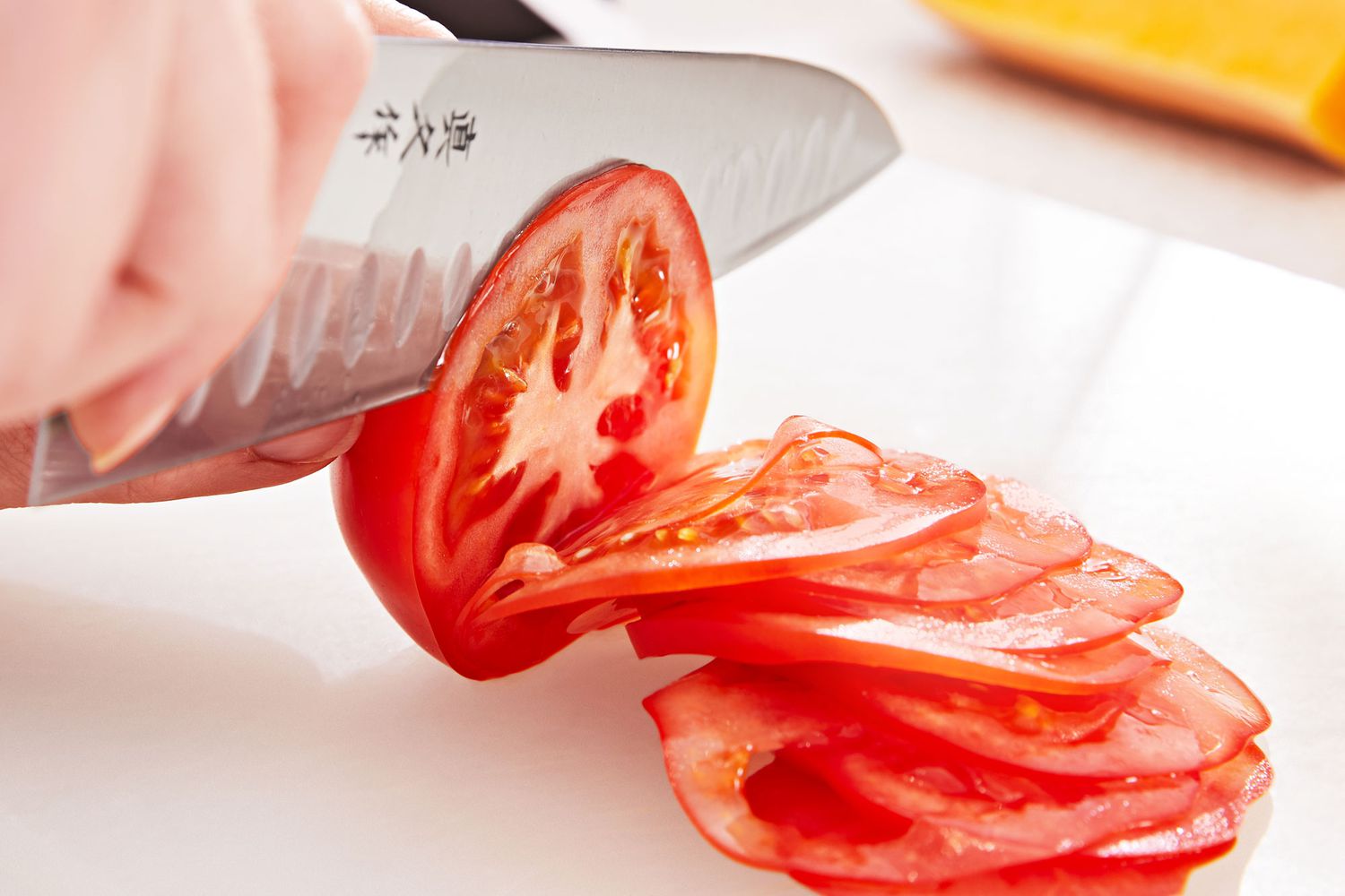 Knife slicing a tomato on a white cutting board