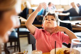 A kid slurps a spaghetti noodle at a restaurant table